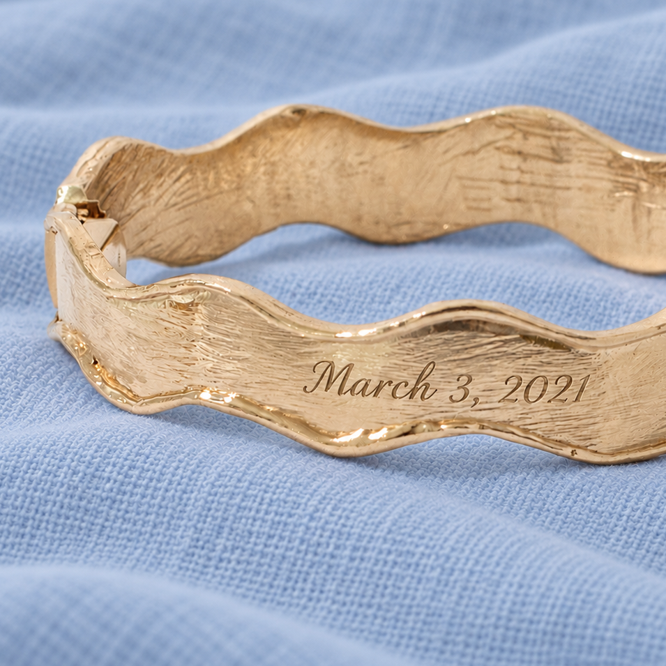 Gold Wavy Bangle with a digital rendering of a date engraved on the outer surface